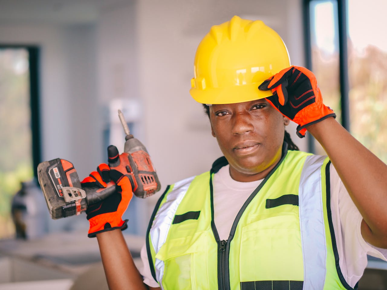 Confident female construction worker wearing safety gear and holding a drill indoors.